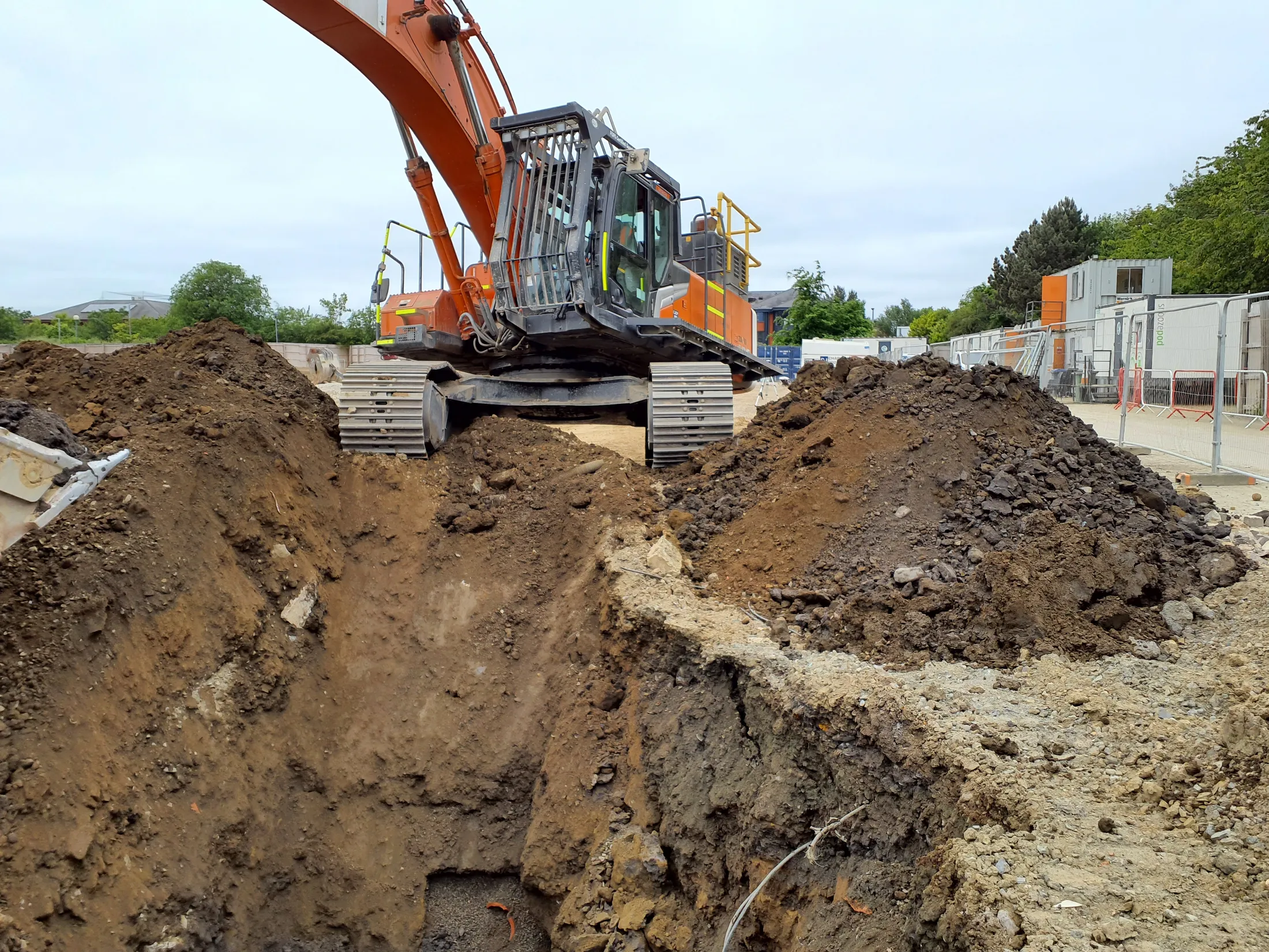An orange excavator beside a deep trench on a construction site.